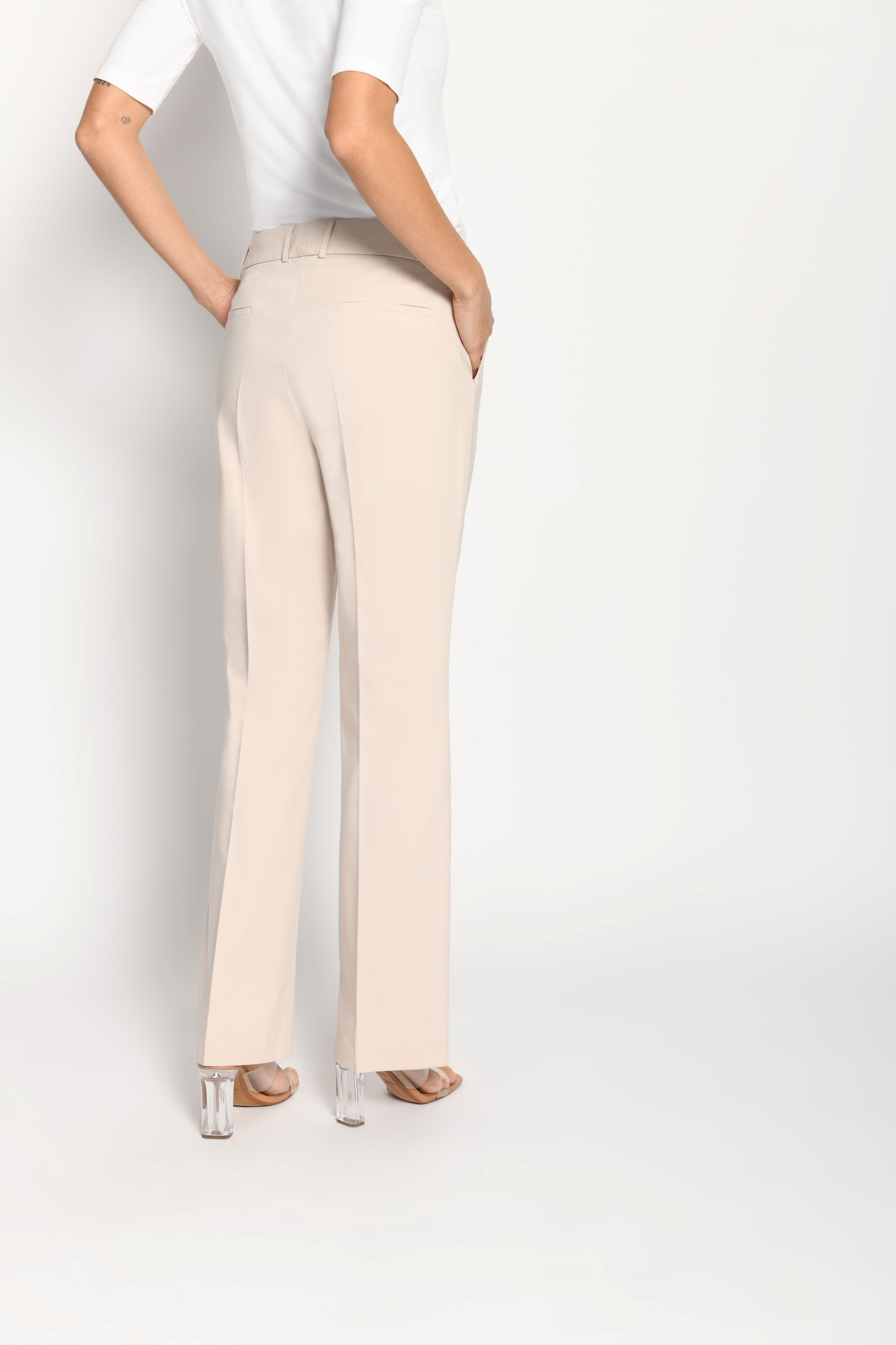 Model trägt beige Stoffhose für Damen mit Buntfalte – stehende Pose, Rückansicht
