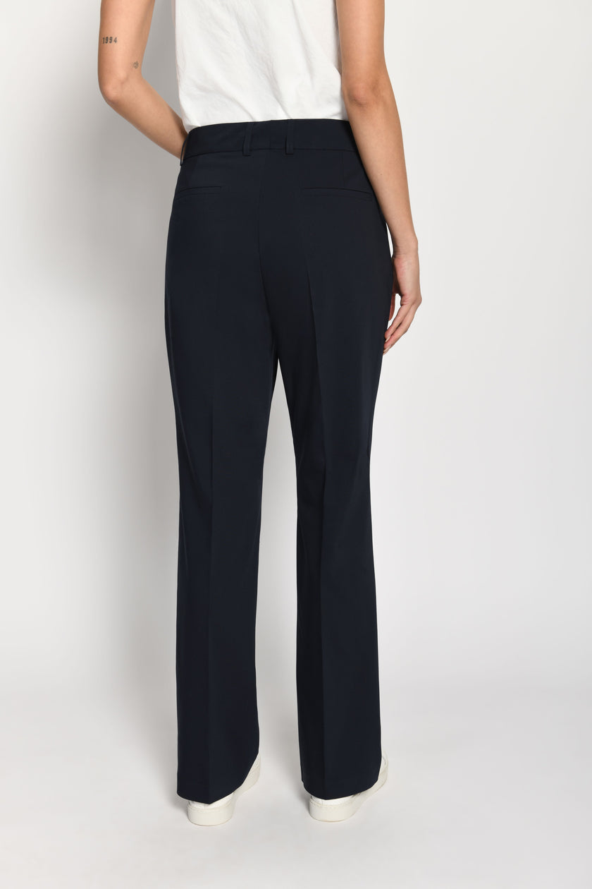 Model trägt dunkelblaue Stoffhose für Damen mit Buntfalte – stehende Pose, Rückansicht