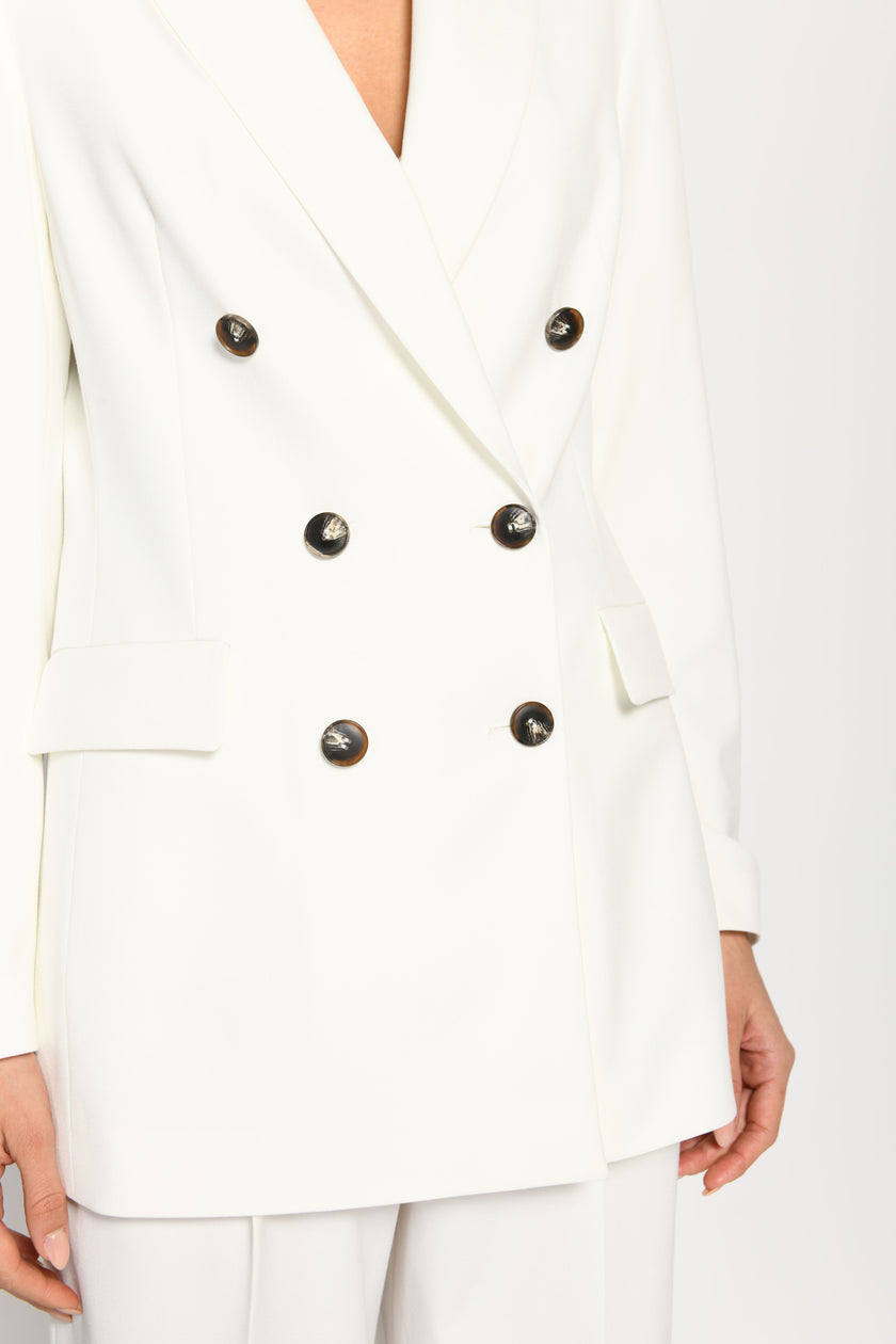 Nahaufnahme der Vorderseite des weißen Blazers mit schwarzem, doppelreihigem Knopfverschluss und Reverskragen.