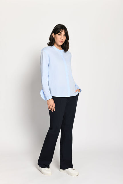 Model trägt hellblaue, locker sitzende Damenbluse mit Rüschen an den Ärmeln – seitliche Pose, Blick nach vorne