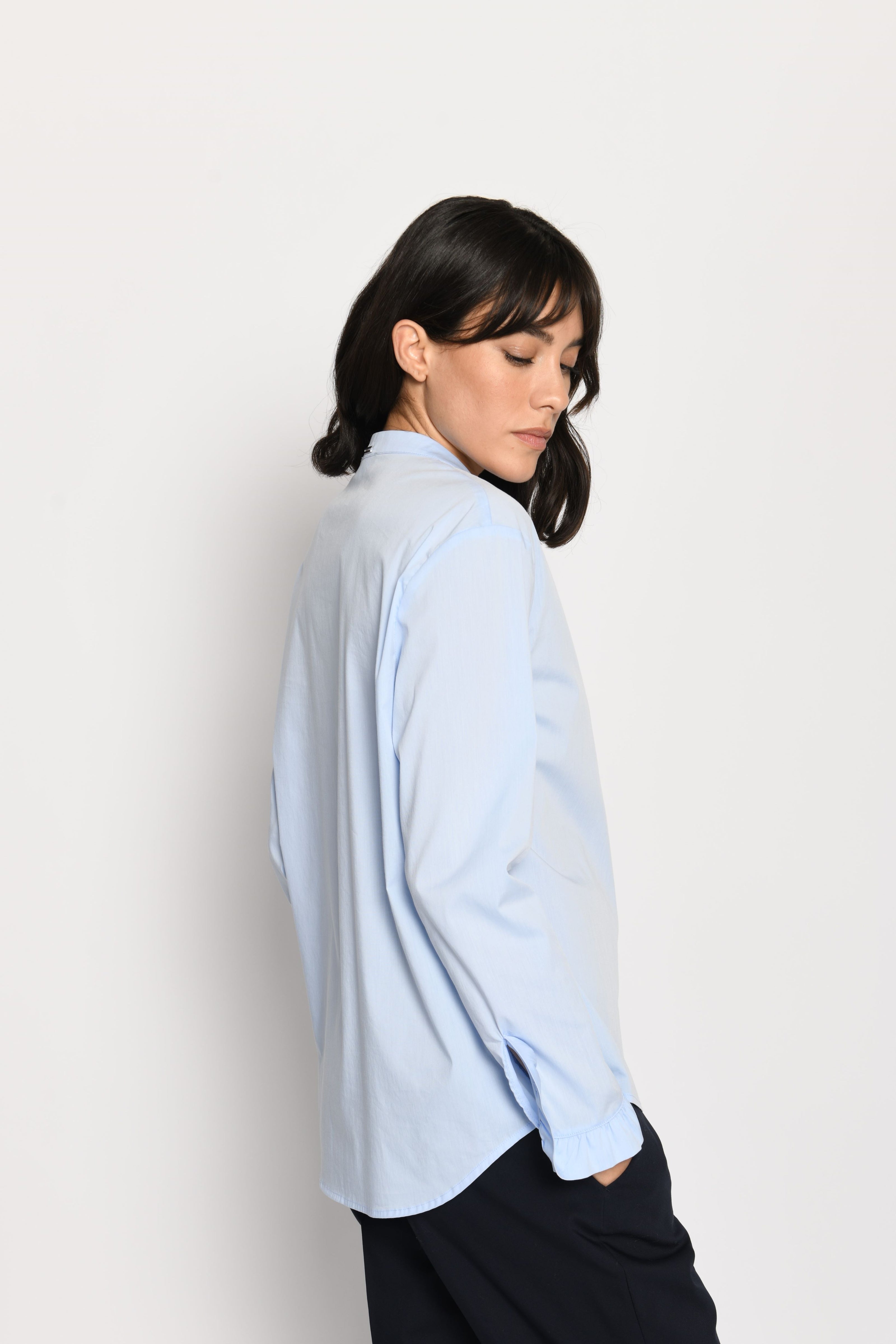 Model trägt hellblaue, locker sitzende Damenbluse mit Rüschen an den Ärmeln – Seitenansicht von links