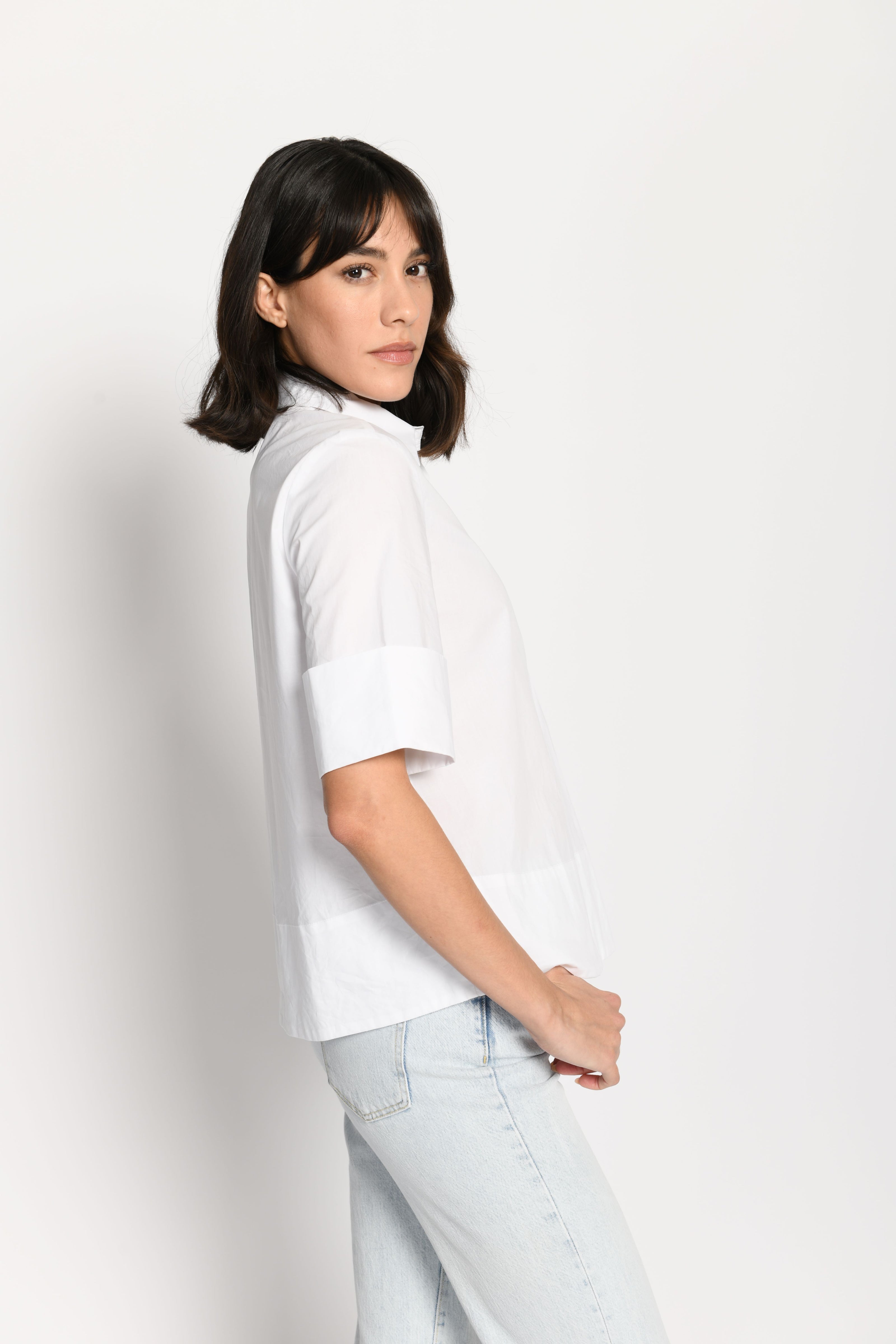 Model trägt kurze kastige Boxy-Bluse in der Farbe Weiß mit kurzen Ärmeln, passend zu einer Jeans – Seitenansicht von links