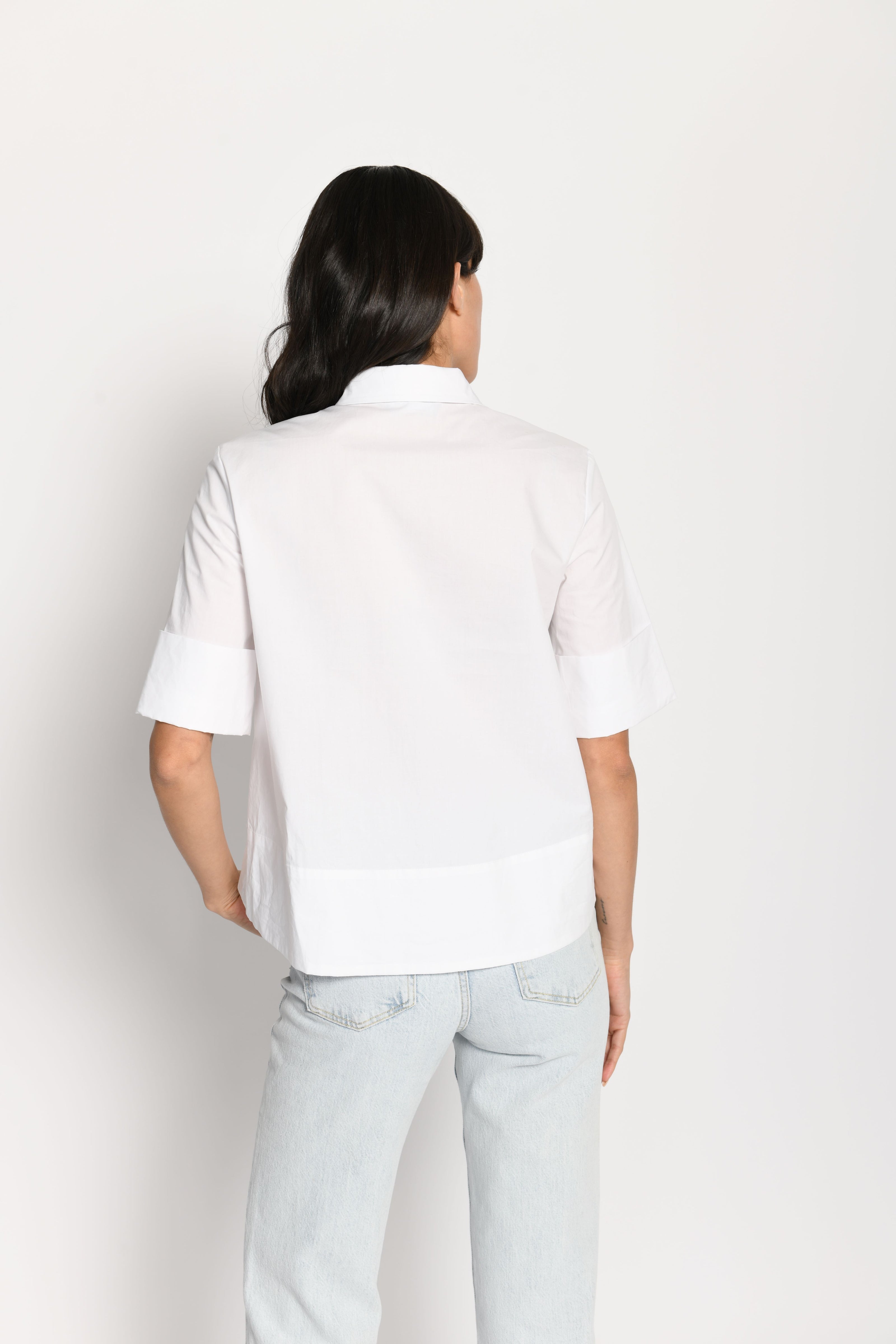 Model trägt kurze kastige Boxy-Bluse in der Farbe Weiß mit kurzen Ärmeln, passend zu einer Jeans – Rückansicht