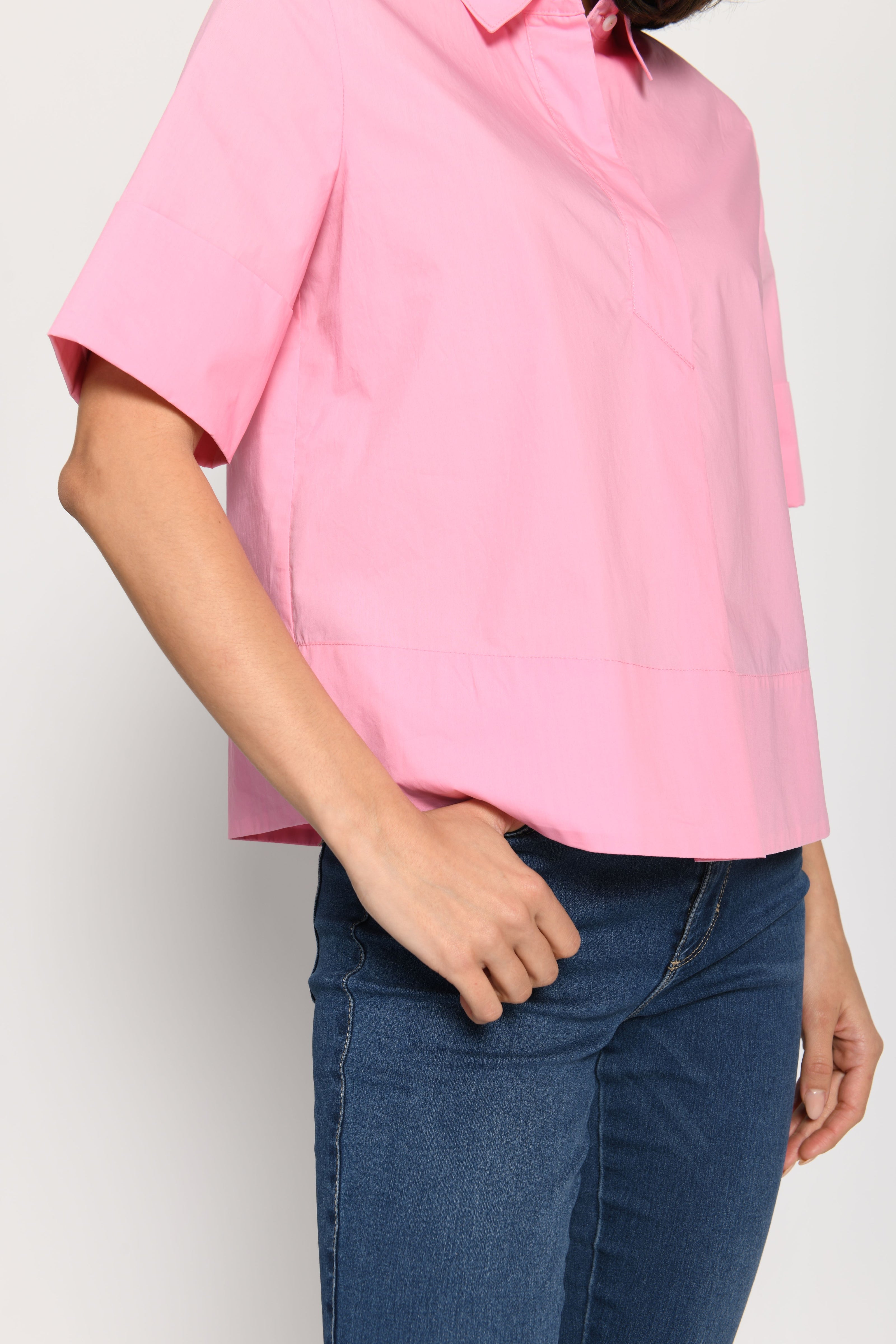 Model trägt kurze kastige Boxy-Bluse in der Farbe Pink mit kurzen Ärmeln, passend zu einer Jeans – Seitenansicht, stehend