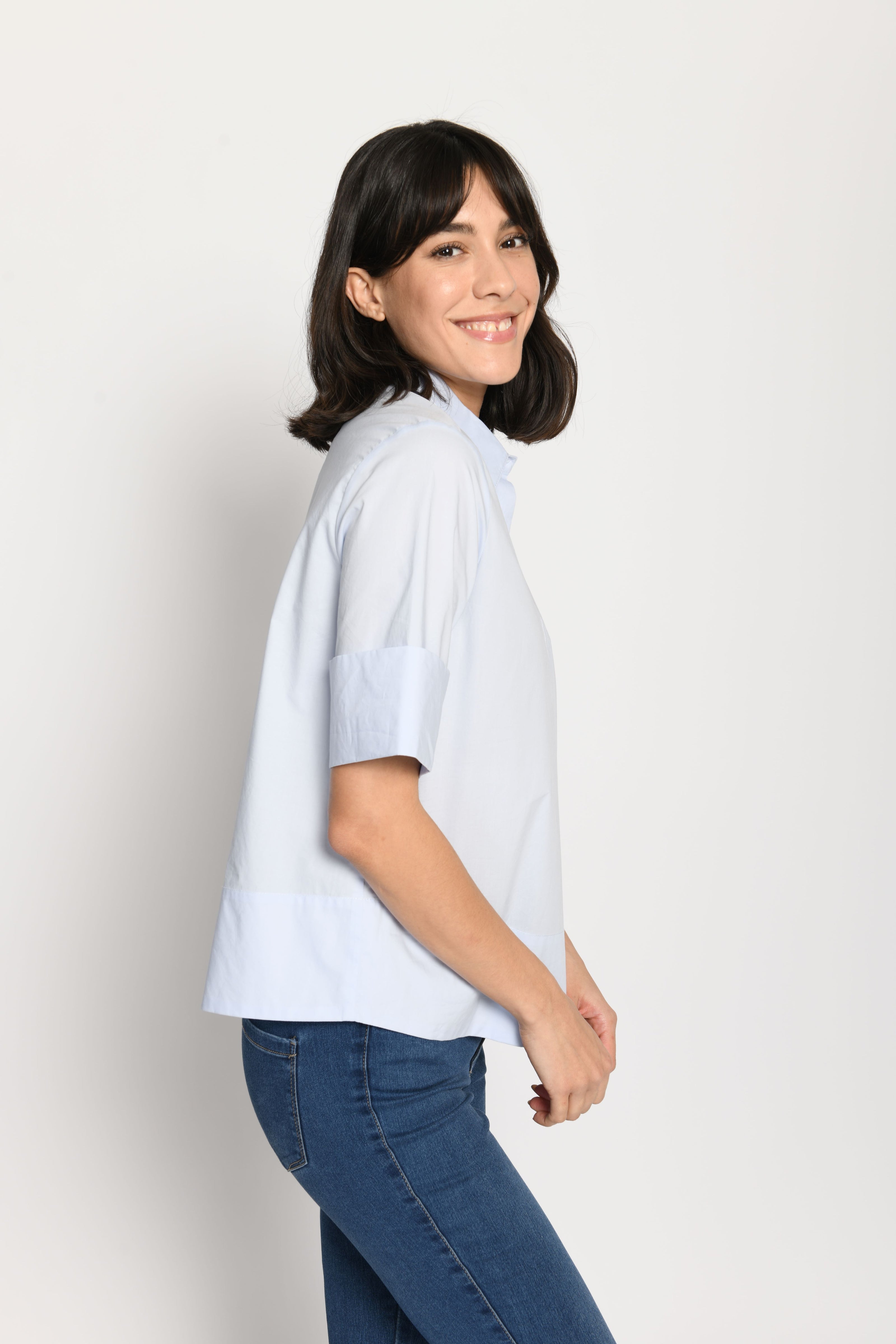 Model trägt kurze kastige Boxy-Bluse in der Farbe Hellblau mit kurzen Ärmeln, passend zu einer Jeans – Seitenansicht von links