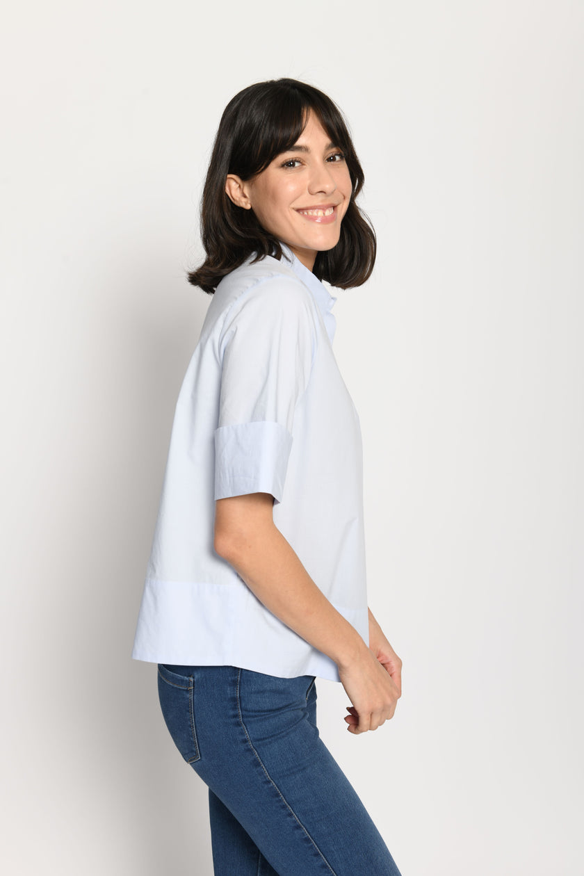 Model trägt kurze kastige Boxy-Bluse in der Farbe Hellblau mit kurzen Ärmeln, passend zu einer Jeans – Seitenansicht von links