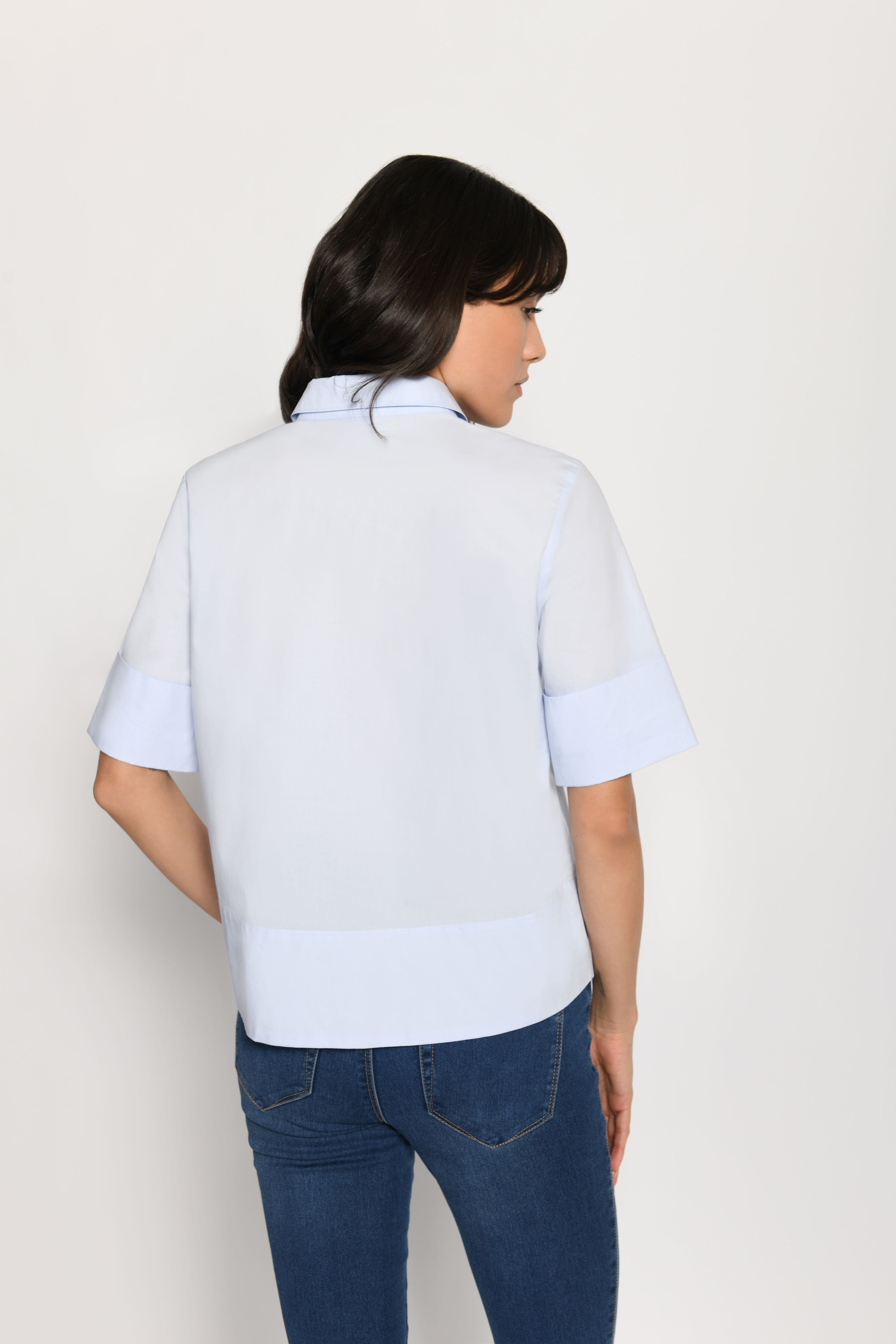 Model trägt kurze kastige Boxy-Bluse in der Farbe Hellblau mit kurzen Ärmeln, passend zu einer Jeans – Rückansicht