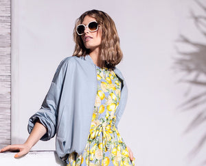 Model trägt ärmelloses, tailliertes Baumwollkleid mit großflächigem Zitronenmuster und passendem hellblauen Blouson. 