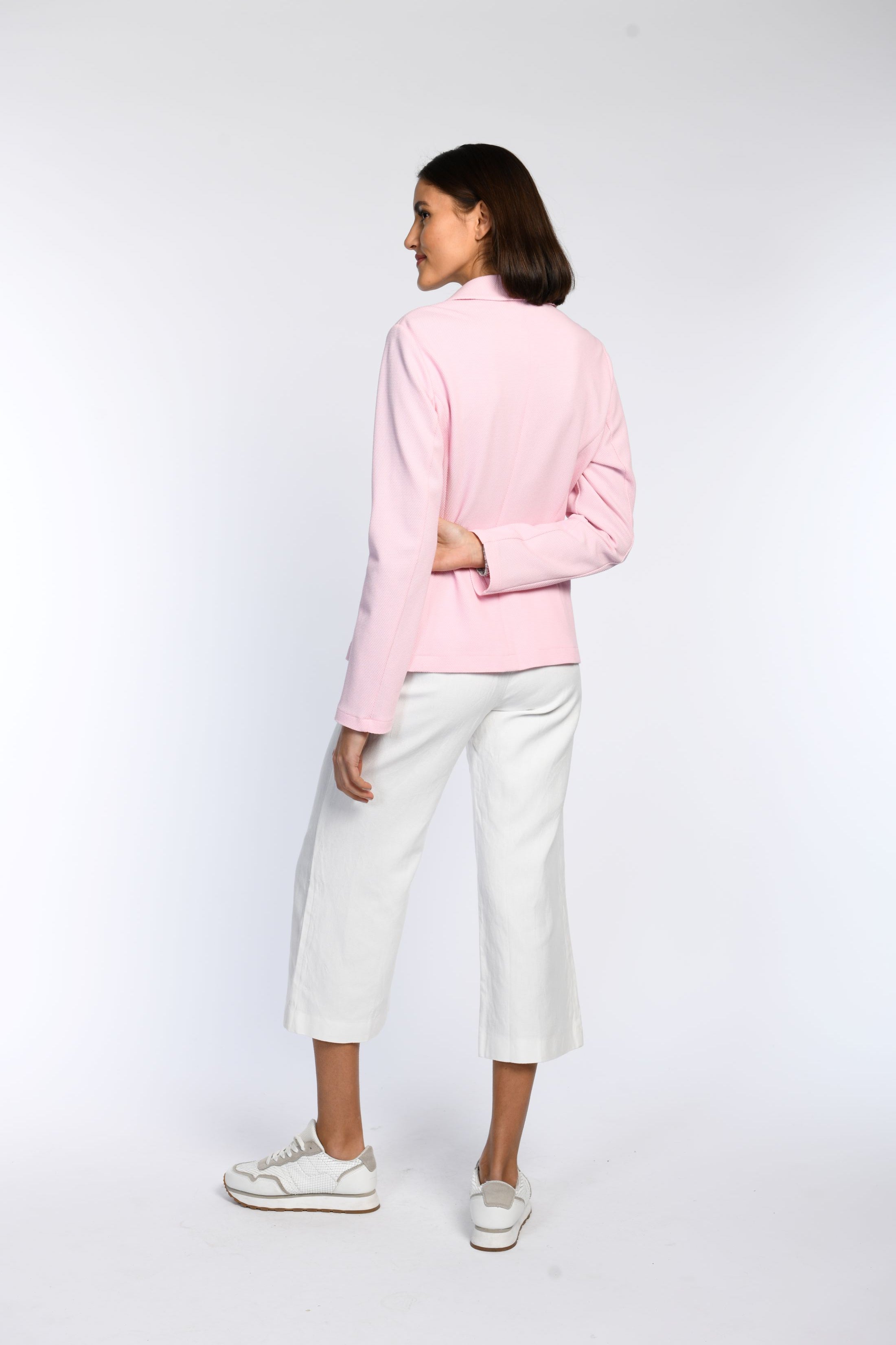 Das Model präsentiert die Rückenansicht eines Blazers aus rosa Jersey.