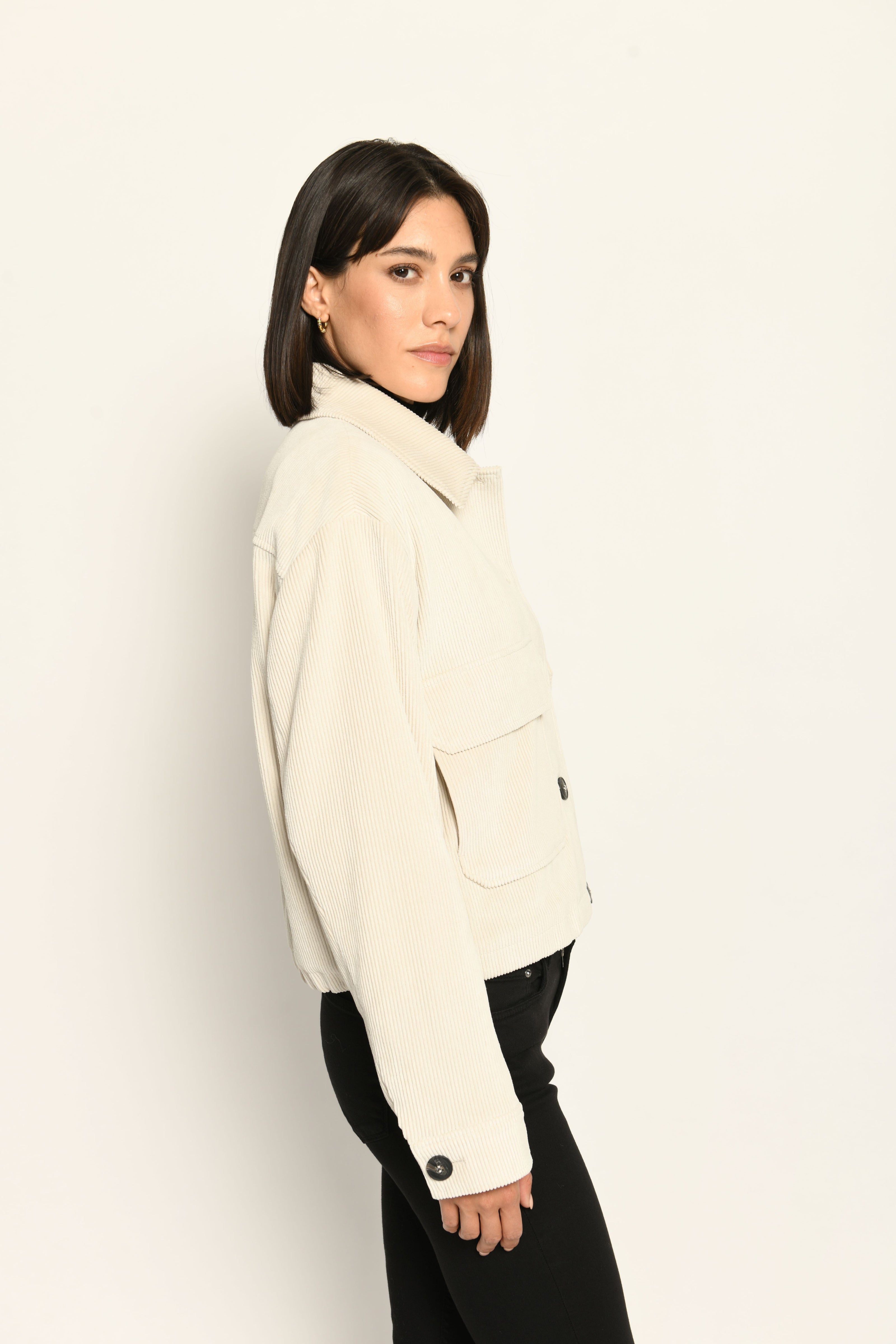 Cord-Blouson in der Farbe Creme mit großen Taschen und schwarzen Knöpfen, kombiniert zu schwarzer Hose – Profilansicht