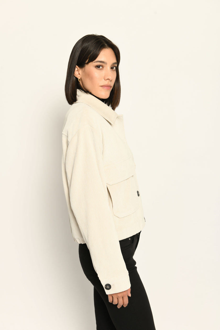 Cord-Blouson in der Farbe Creme mit großen Taschen und schwarzen Knöpfen, kombiniert zu schwarzer Hose – Profilansicht