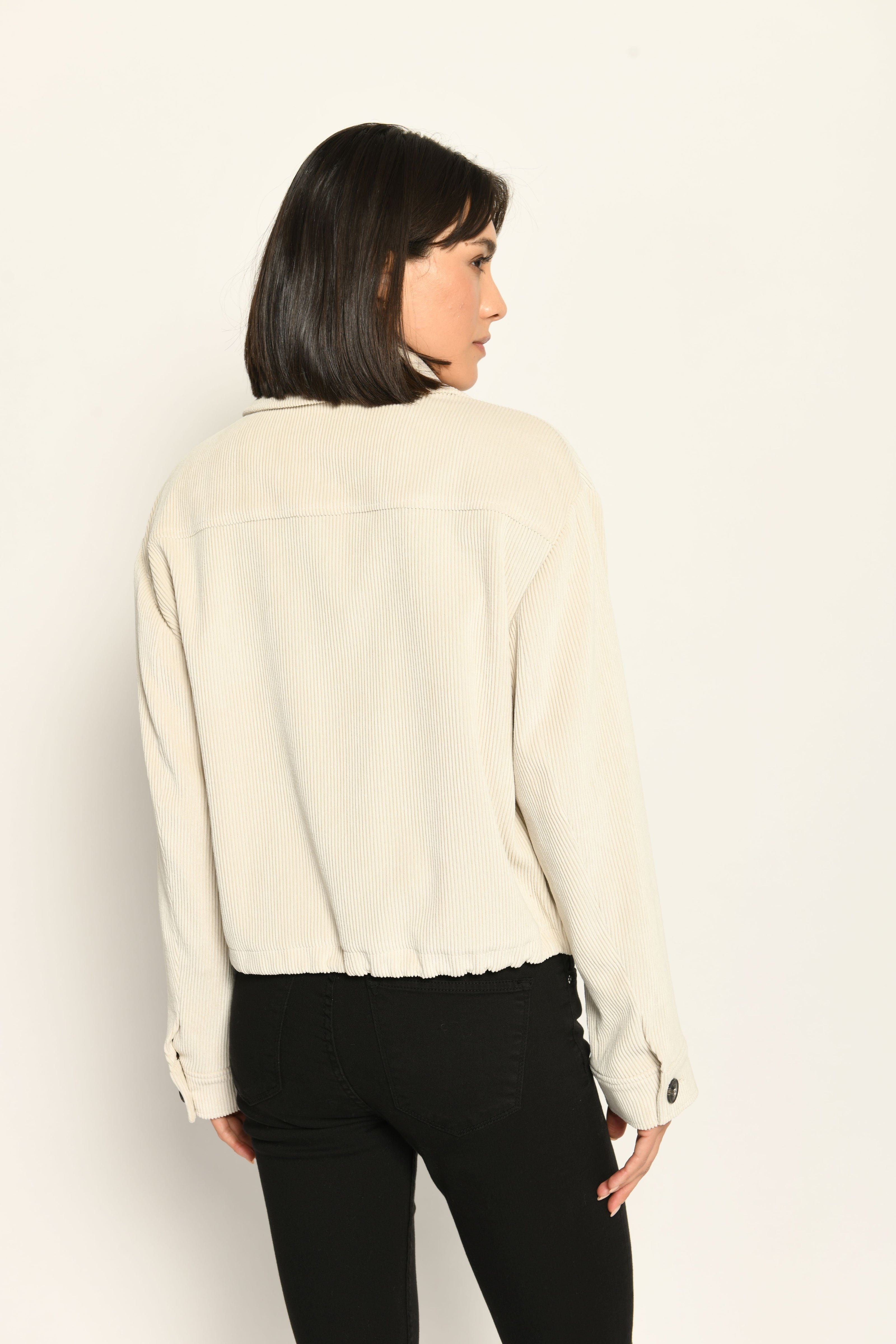 Cord-Blouson in der Farbe Creme mit großen Taschen und schwarzen Knöpfen, kombiniert zu schwarzer Hose – Rückansicht