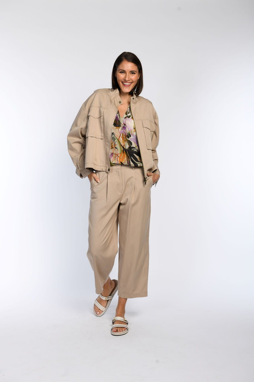 Model trägt ein braunes, locker geschnittenes Blouson zu einer locker geschnittenen  Hose und einer leichten Bluse mit Print.