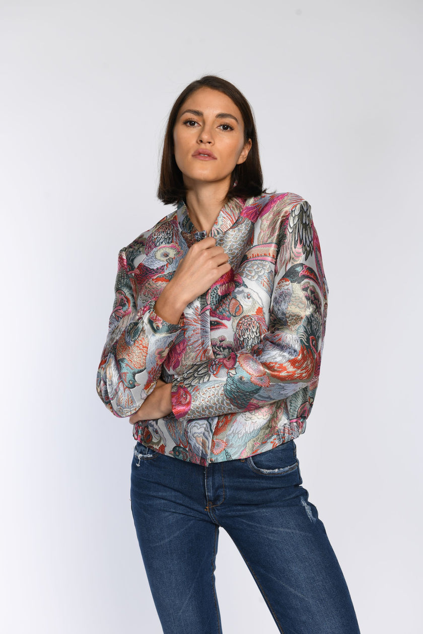 Model trägt ein geschlossenes, buntes Blouson mit zartem Glanz und Vogelmuster.