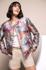 Model trägt locker geschnittenes Blouson mit buntem Vogelmuster, zartem Glanz und elastischem Ärmelbündchen.