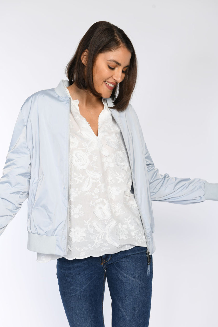 Model kombiniert weiße Bluse mit 3D-Bluetenstickerei mit blauem Blouson und Jeans.