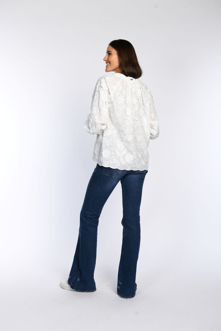 Rückenansicht: Model trägt weiße Bluse mit floraler 3D-Stickerei und Saum mit Wellenkante.