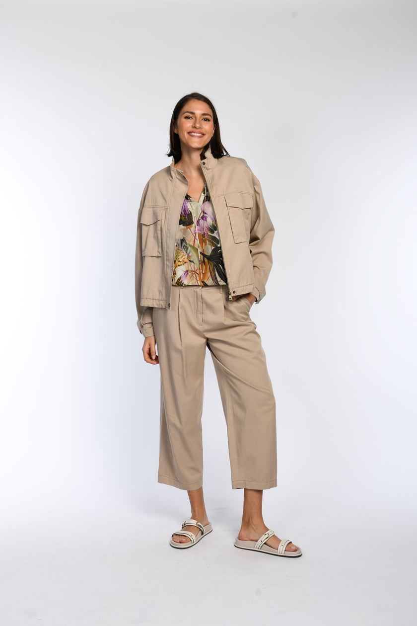 Model trägt Bluse mit floralem Druck, kombiniert mit beiger Hose und Blouson.