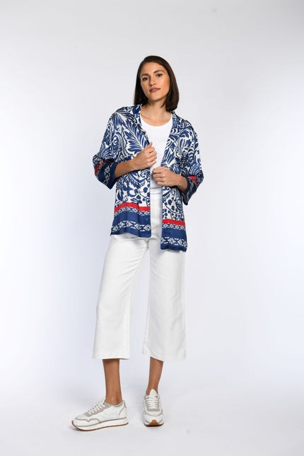 Vorderansicht einer blau bedruckten Bluse mit roten Akzenten, kombiniert zu einem All-White-Look.