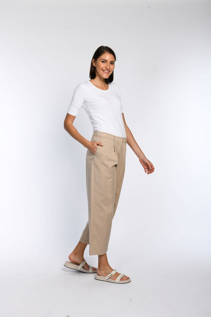 Model trägt eine verkürzte Hose mit weitem Bein, Bundfalten und schrägen Eingriffstaschen in Beige.