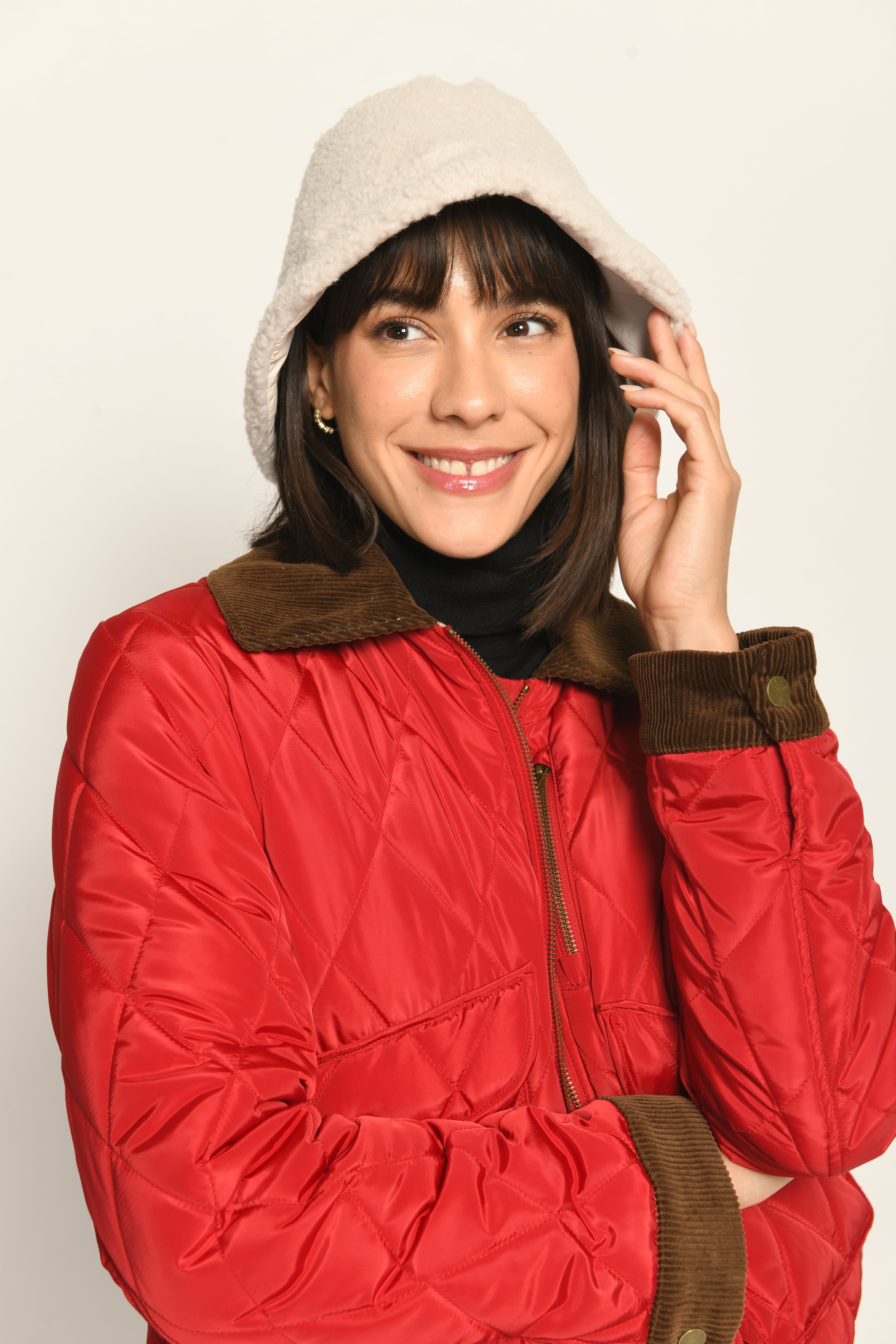 Model trägt Hut aus flauschigem cremefarbenem Teddy-Webpelz, lässig kombiniert zu einer roten Jacke – Vorderansicht
