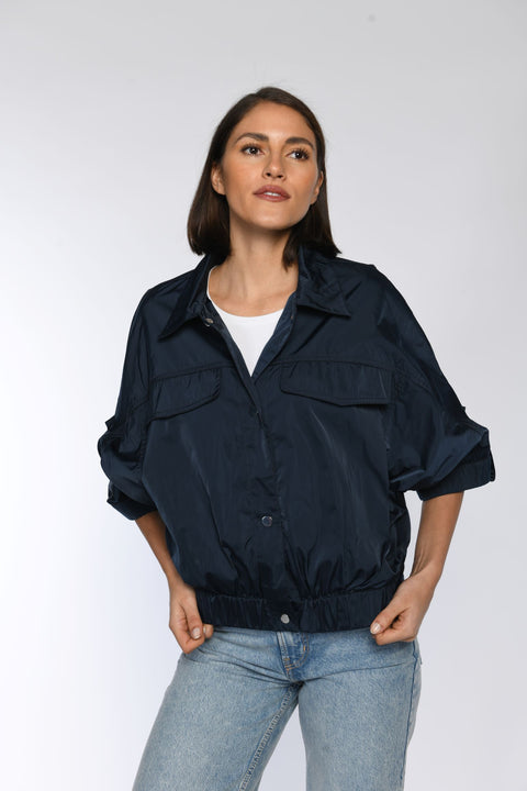 Modell trägt blaue Sommerjacke, geschlossen mit Druckknopfverschluss und Pattentaschen auf Brusthöhe.