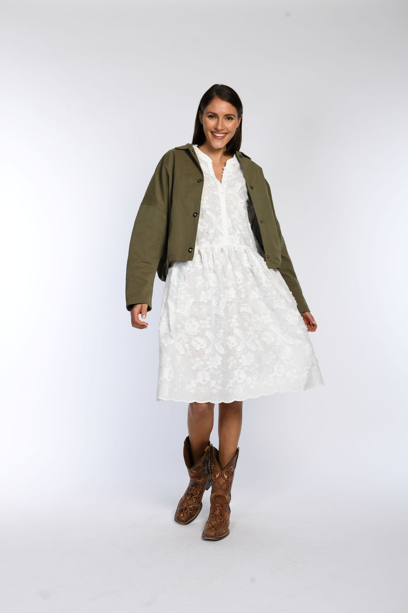 Model trägt offene olivfarbene Jacke, kombiniert mit weißem Kleid und Cowboyboots. 