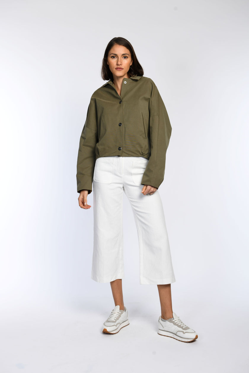 Model trägt geschlossene olivfarbene Jacke mit Druckknopfverschluss, kombiniert mit weißer Hose.