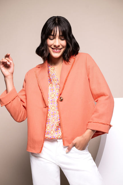 Model trägt kastig geschnittene Kastenjacke in Orange mit Fransendetails.