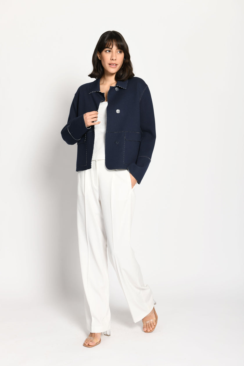 Model trägt dunkelblaue Kastenjacke, passend kombiniert zur weißen Stoffhose und einem weißen Top – Vorderansicht.