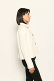 Model trägt weiße Kastenjacke für Damen aus Scuba mit schwarzen großen Knöpfen und aufgesetzten Taschen – Profilansicht