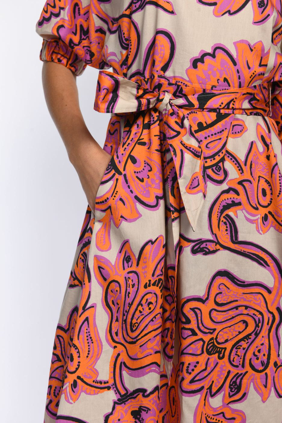 Detailansicht des Kleides mit leuchtendem Muster, Bindegürtel in der Taille und versteckten Nahttaschen.