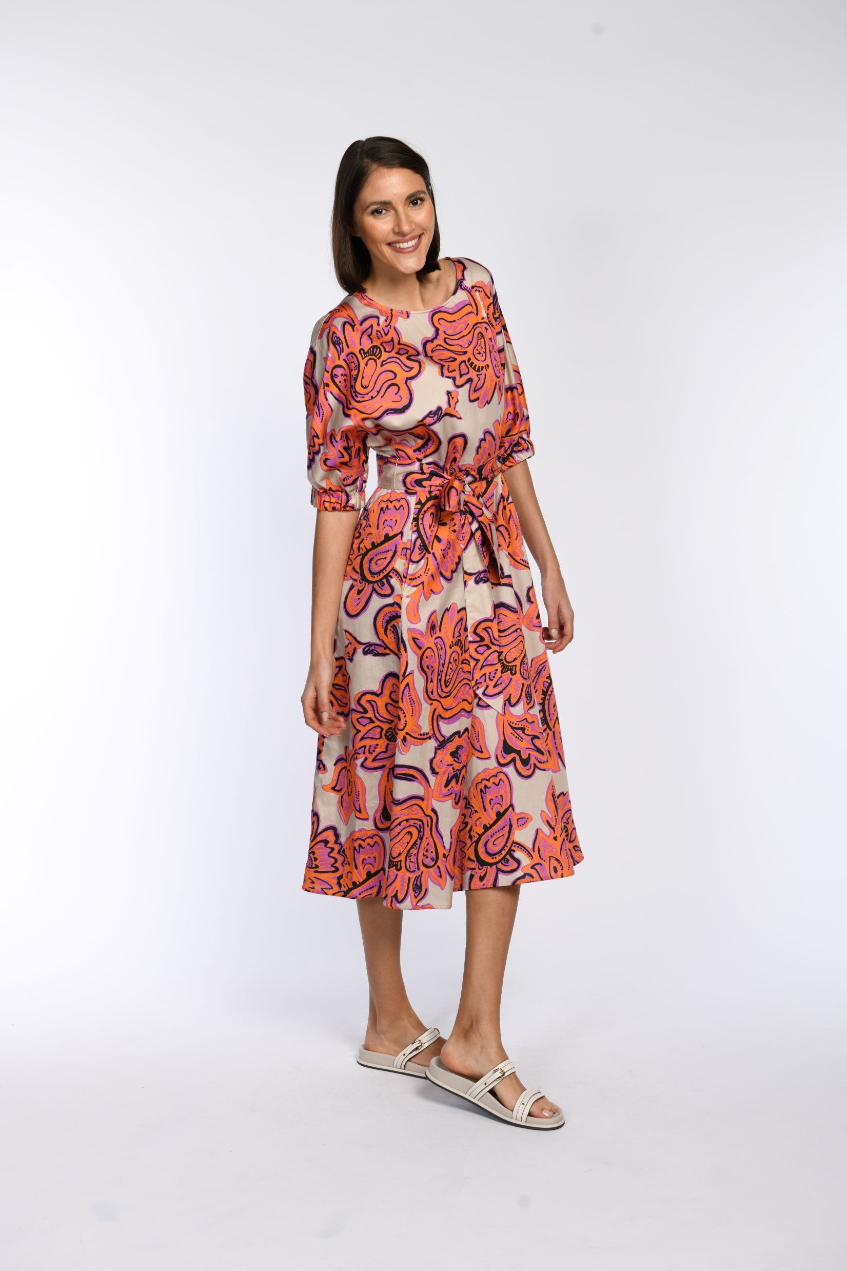 Model trägt locker fallendes Sommerkleid aus 100 % Baumwolle mit floralem Druck in Pink und Orange inklusive Bindegürtel.