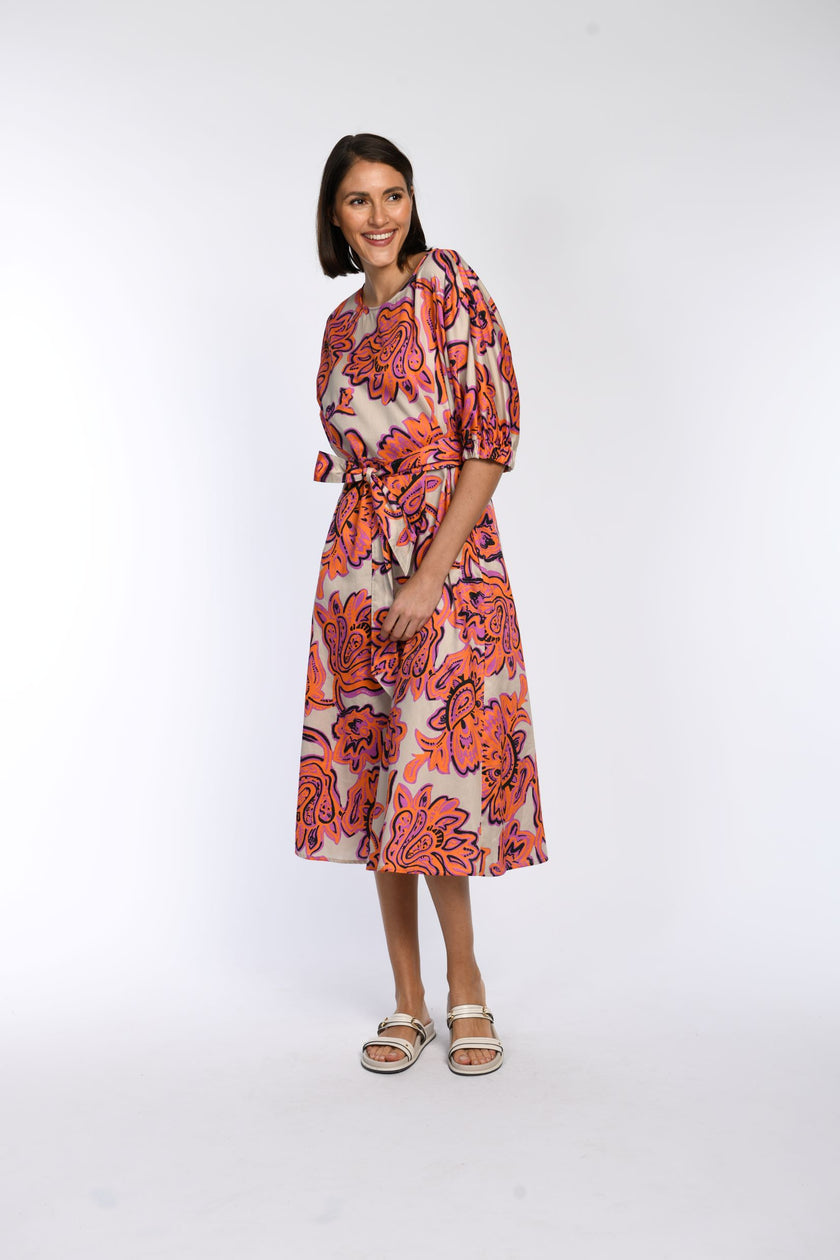 Model trägt Sommerkleid aus 100 % Baumwolle mit floralem Druck in Pink und Orange, sichtbarer Bindegürtel.