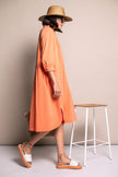Oranges, leichtes Sommerkleid kombiniert mit farblich abgestimmten Sandalen, beigem Strohhut und beiger Basttasche.