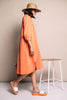 Oranges, leichtes Sommerkleid kombiniert mit farblich abgestimmten Sandalen, beigem Strohhut und beiger Basttasche.