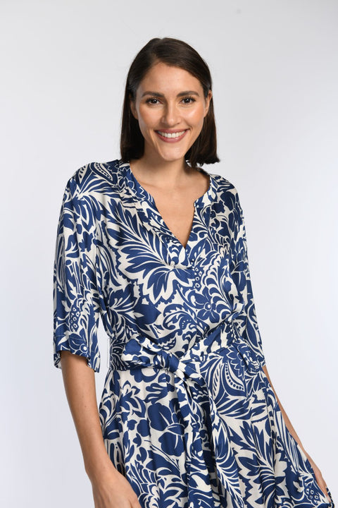 Detailaufnahme zeigt Baumwollkleid mit blauem Blumendruck, V-Ausschnitt, Halbarm und Bindegürtel.  