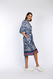 Model trägt knielanges Baumwollkleid mit blauem Blumendruck und hat die Hände in den Nahttaschen versteckt.