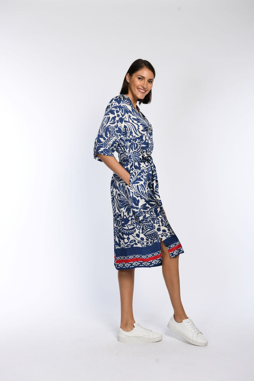 Model trägt knielanges Baumwollkleid mit blauem Blumendruck und hat die Hände in den Nahttaschen versteckt.