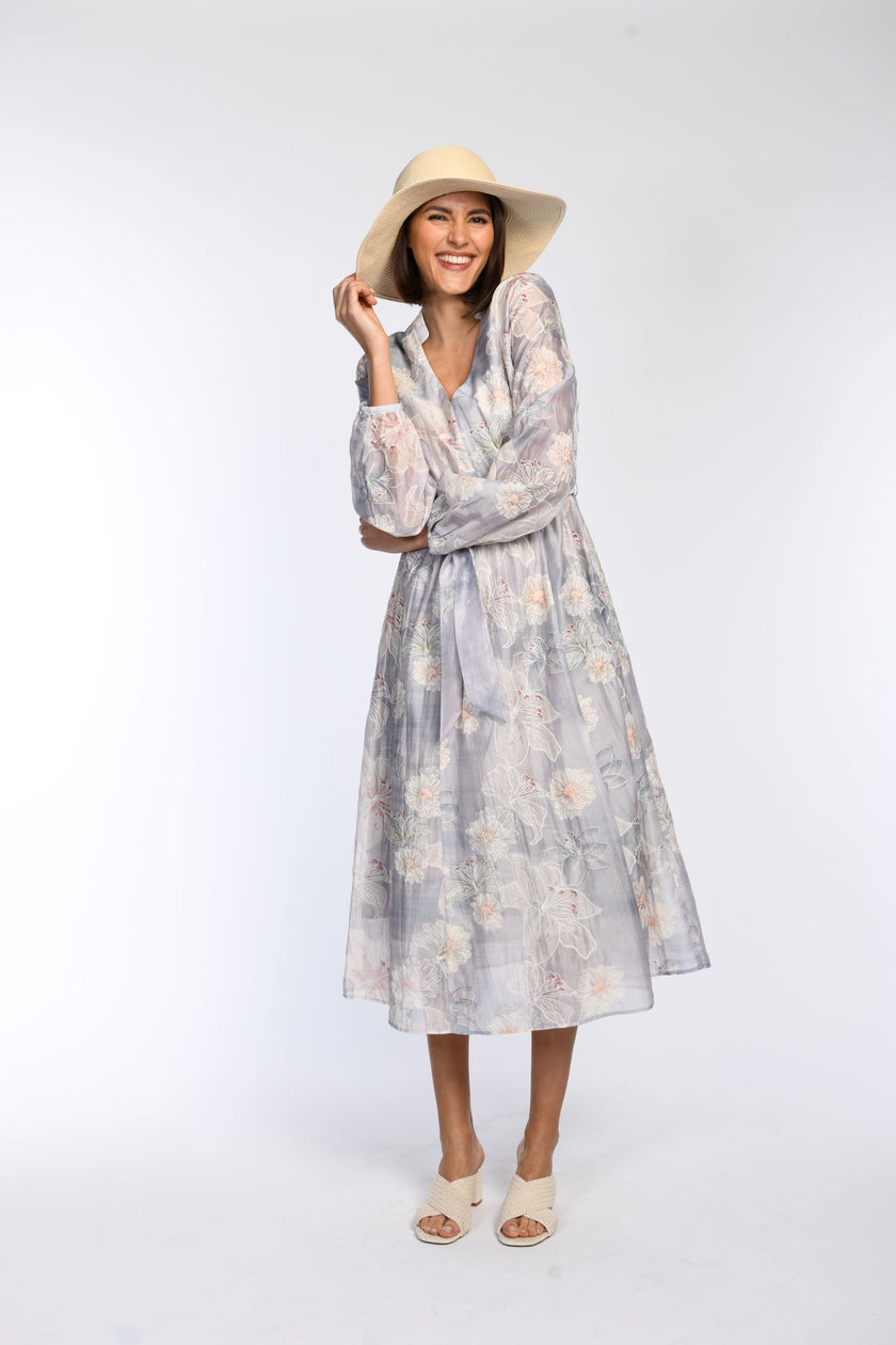 Model trägt bedrucktes, langärmeliges Maxikleid mit zartem Pastellprint, kombiniert mit Basthut und offenen Schuhen.
