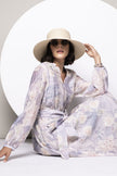 Model trägt bedrucktes, langärmeliges Kleid mit zartem Pastellprint, kombiniert mit Basthut und Sonnenbrille.