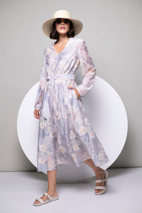 Model trägt bedrucktes, langärmeliges Kleid mit zartem Pastellprint, kombiniert mit Basthut und offenen Schuhen.