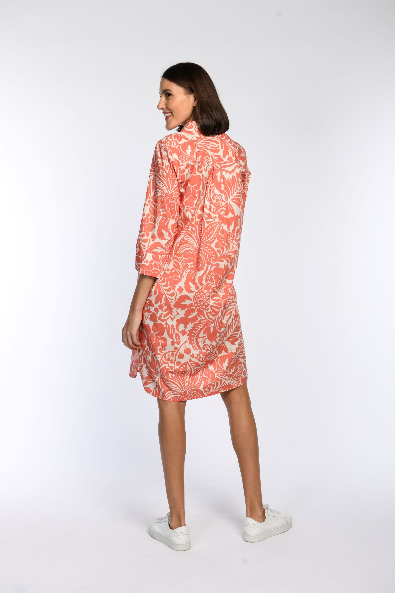 Orangefarbenes, locker fallendes, knielanges, weiß gemustertes Hemdblusenkleid in Rückansicht.