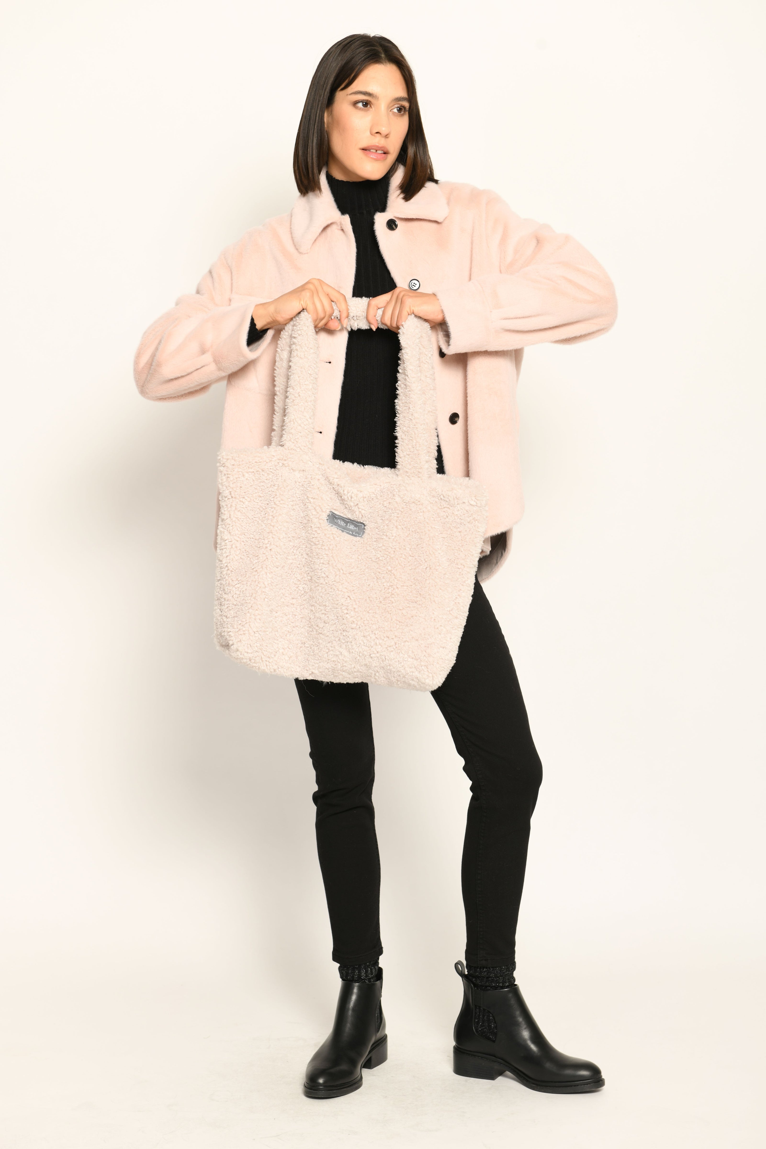 Model trägt Umhängetasche aus Webpelz in der Farbe Creme mit Reißverschluss und zwei langen Henkeln – Vorderansicht.