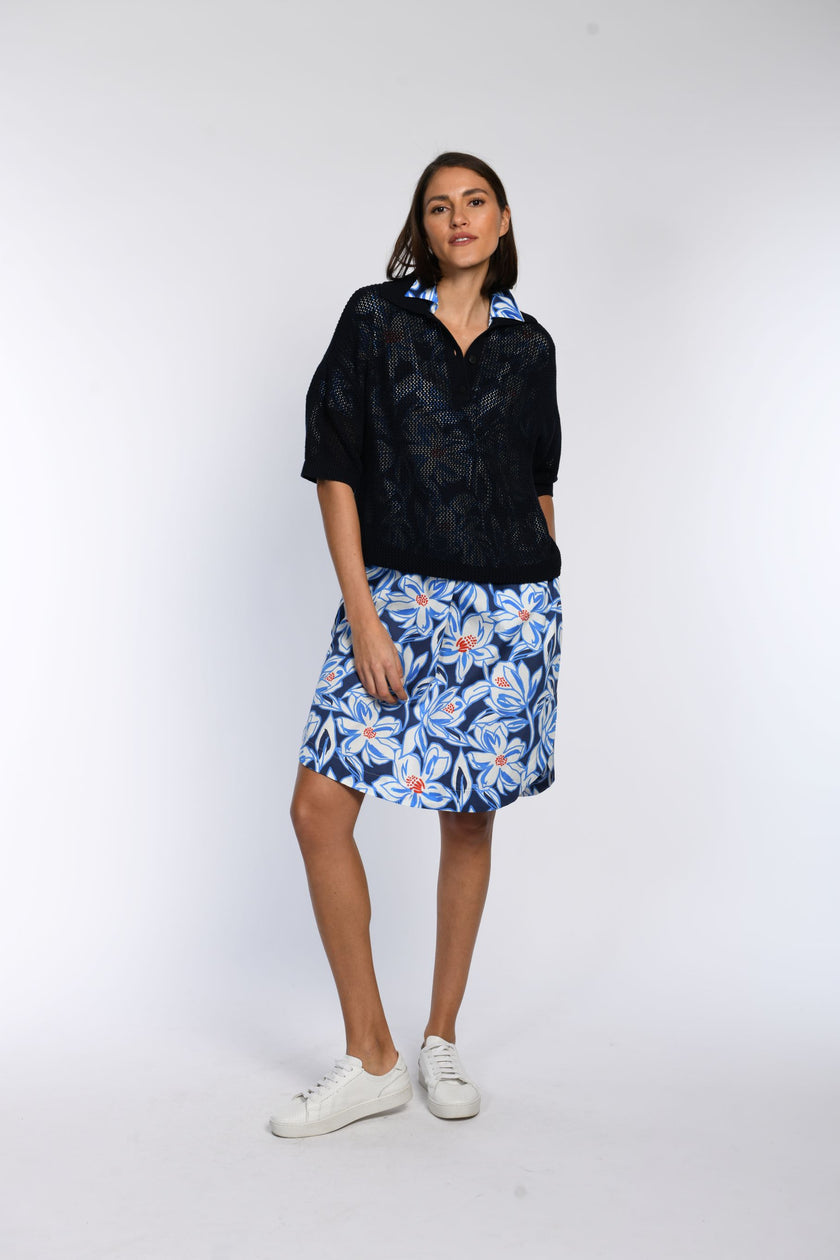 Model trägt ein locker geschnittenes,leicht durchsichtiges Poloshirt über einem sommerlichen Kleid.