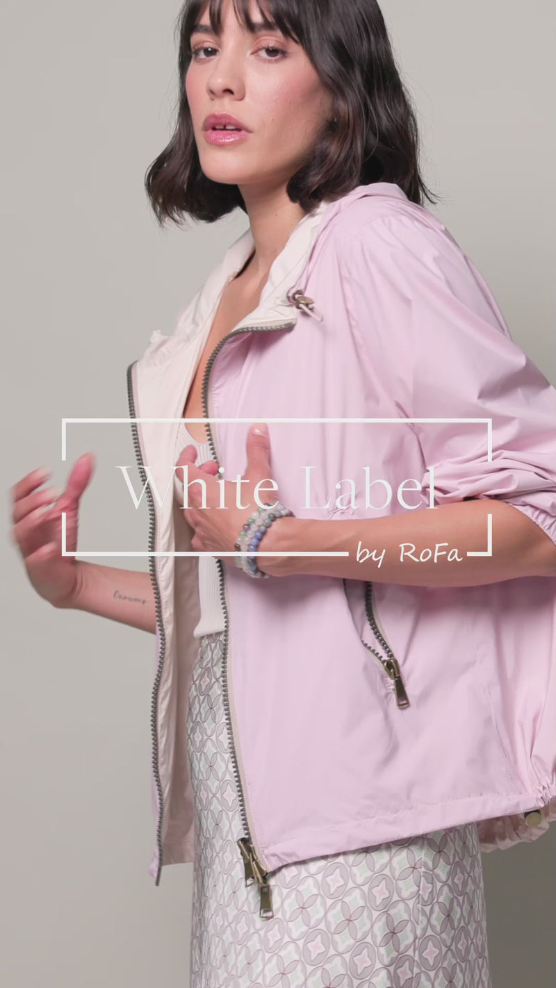 Model trägt Wendejacke mit Kapuze. Eine Seite in Rosa, die Wendeseite in hellem Beige. Mit Tunnelzug am Saum.