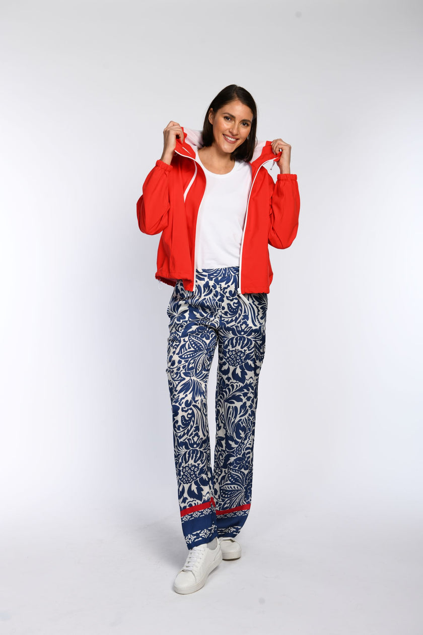 Model trägt eine offene rote Regenjacke mit Kapuze, kombiniert mit gerade geschnittener Palazzo-Hose.