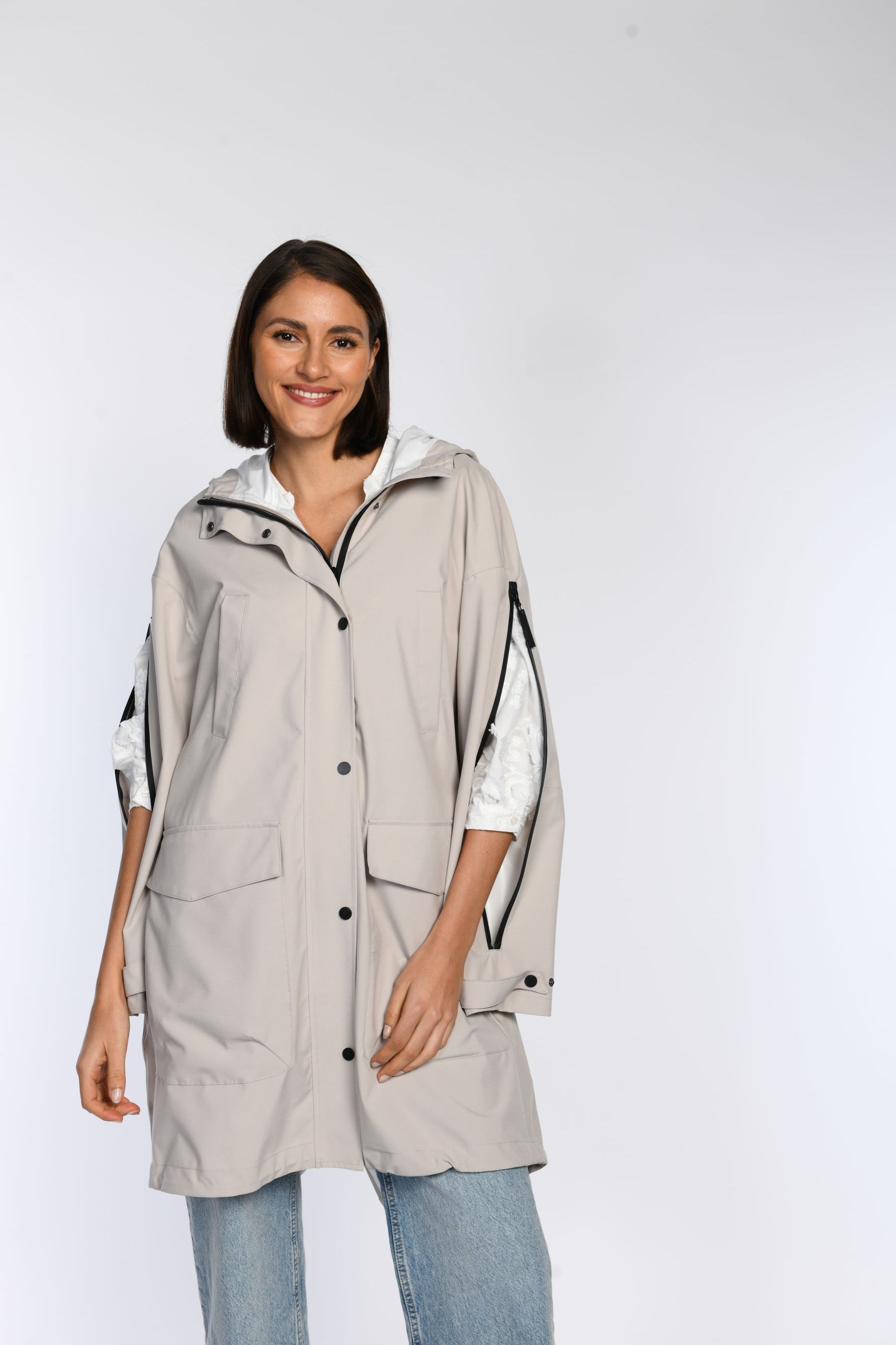Beiger Regenparka in der Vorderansicht, geschlossen getragen. Die Armschlitze sind offen und bieten Bewegungsfreiheit.