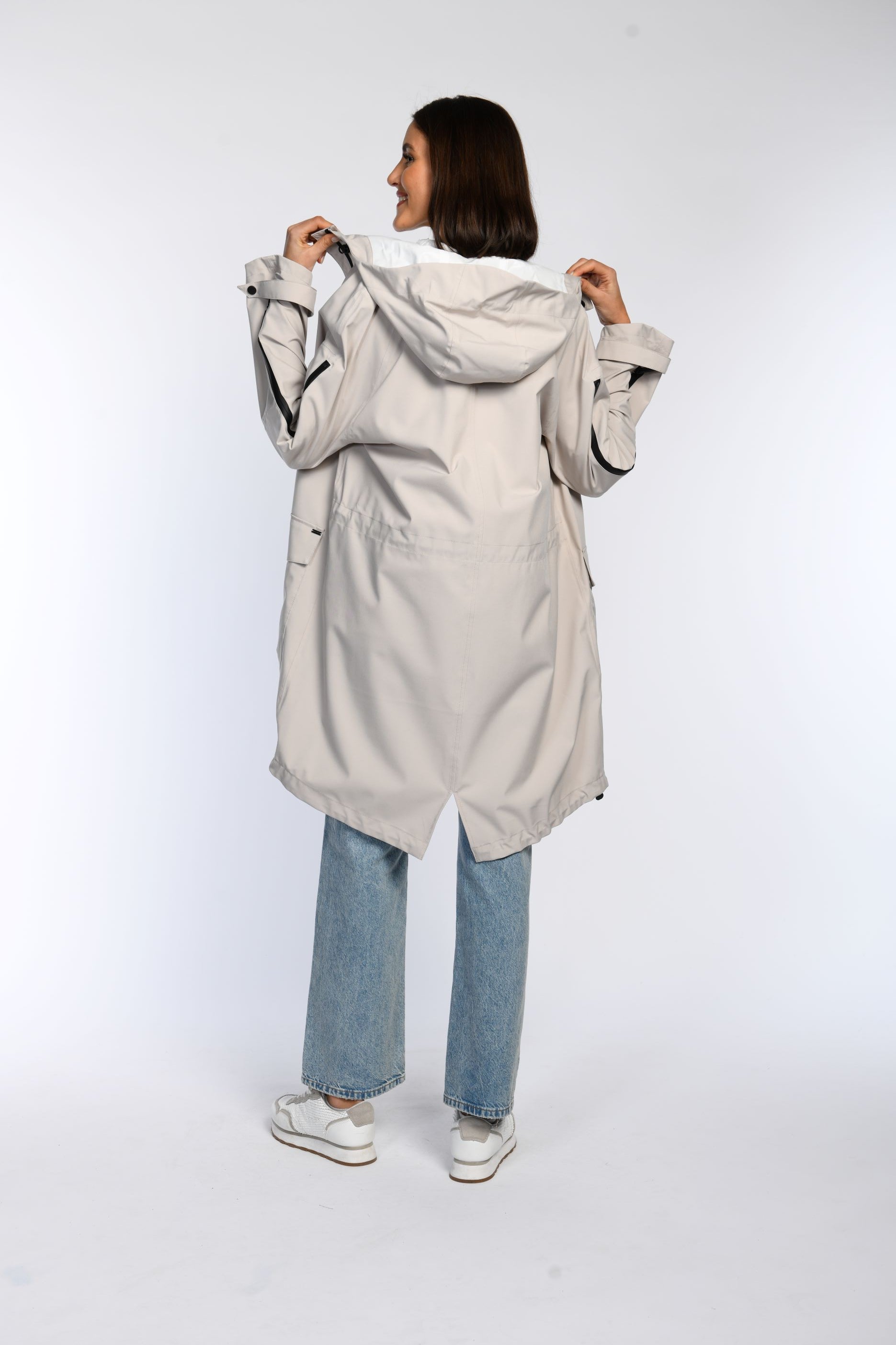 Rückansicht eines Models in einem beigen Regenparka mit Kapuze.