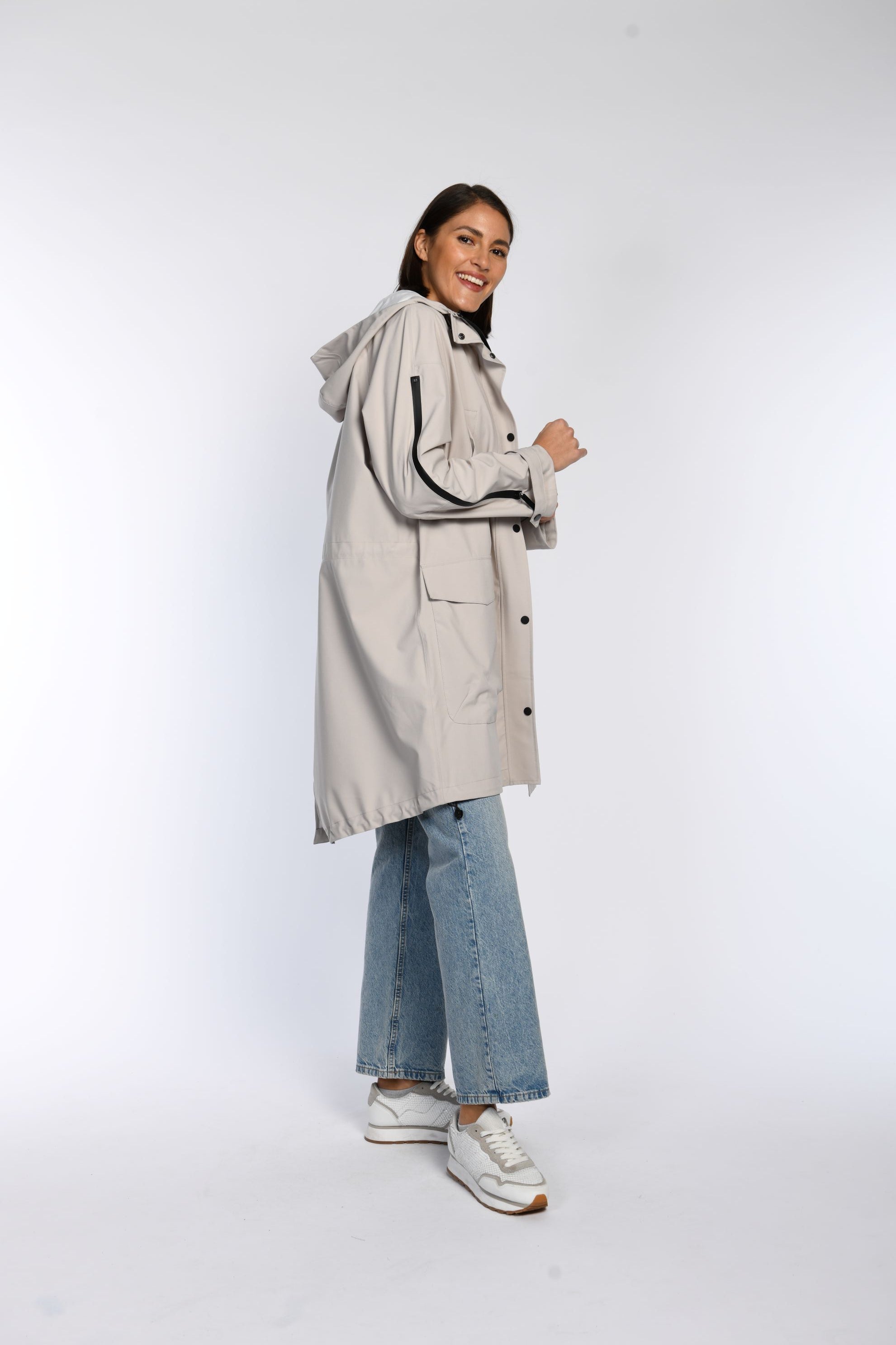 Seitenansicht eines Models in einem beigen Regenparka mit Kapuze. 